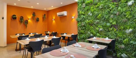 Un restaurante con mesas dispuestas para comer, una pared cubierta de vegetación e iluminación empotrada.