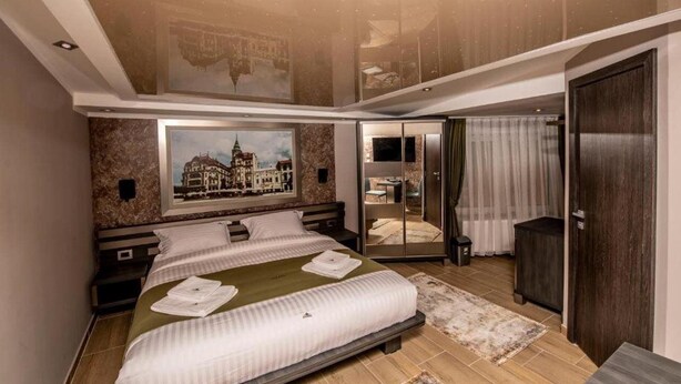 Un dormitorio moderno con una cama grande, un espejo y un cuadro con una vista urbana.