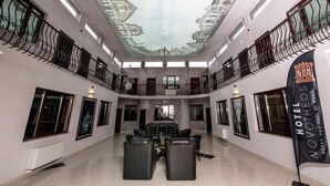Un hall de hotel con techo alto, una zona de estar central y un cartel que dice "HOTEL NOVOTEOOS".