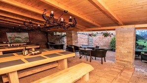 Un área de comedor al aire libre con bancos y mesas de madera, una pared de ladrillo y un pilar de piedra.