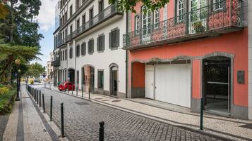 A cobblestone street with buildings, a red car, and a sign for 'Dona Media'.