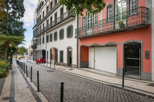 A cobblestone street with buildings, a red car, and a sign for 'Dona Media'.