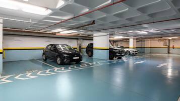 Un parking à plusieurs niveaux, avec des flèches directionnelles clairement indiquées au sol, plusieurs voitures stationnées et un panneau indiquant « Hôtel Madeira ».