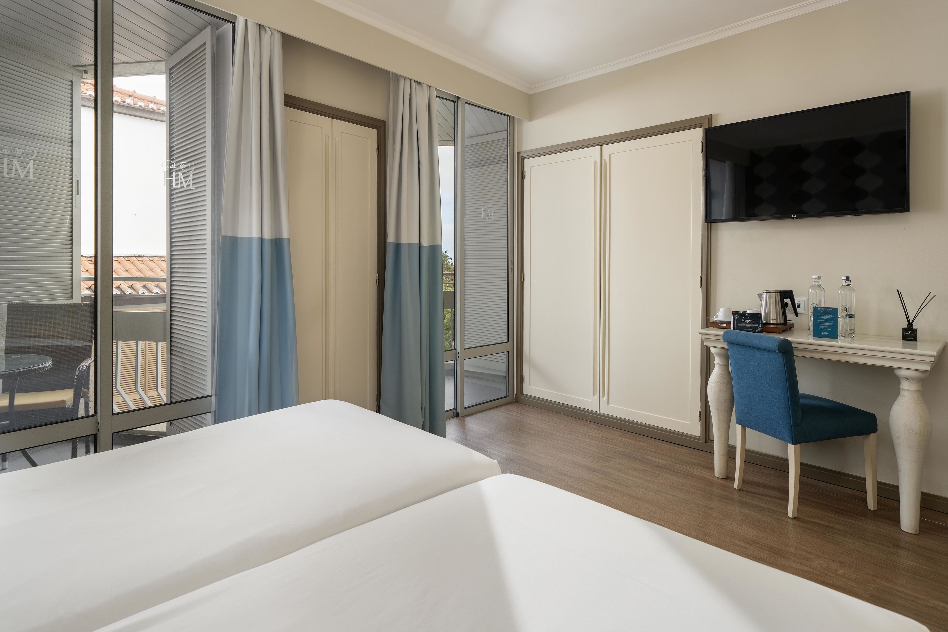 Habitación de hotel con cama, escritorio con silla, televisor y vista al exterior.
