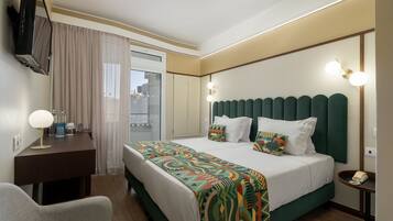 Quarto de hotel com cama, escrivaninha, cadeira, televisão e telefone.
