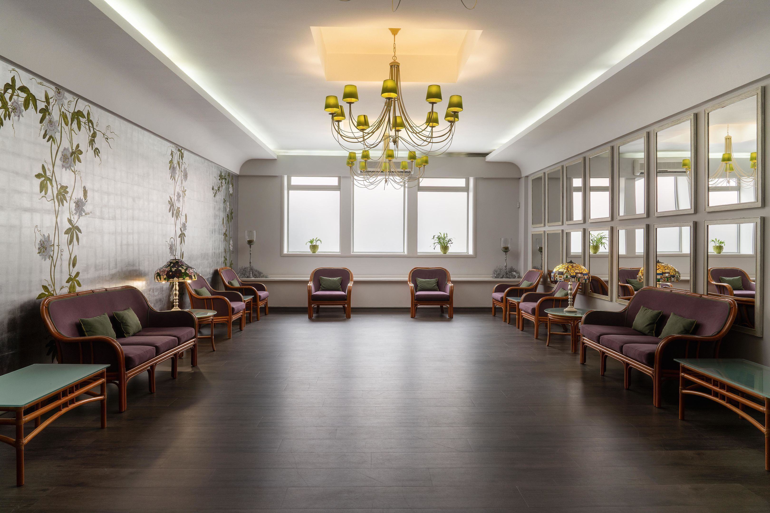 A spacious room with a large chandelier, multiple windows, and a row of sofas and chairs.
