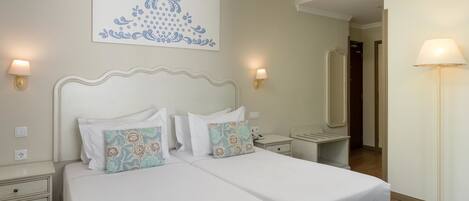 A double bed with white bedding and floral-patterned pillows, bedside tables with lamps, a wall-mounted artwork, and a mirror.