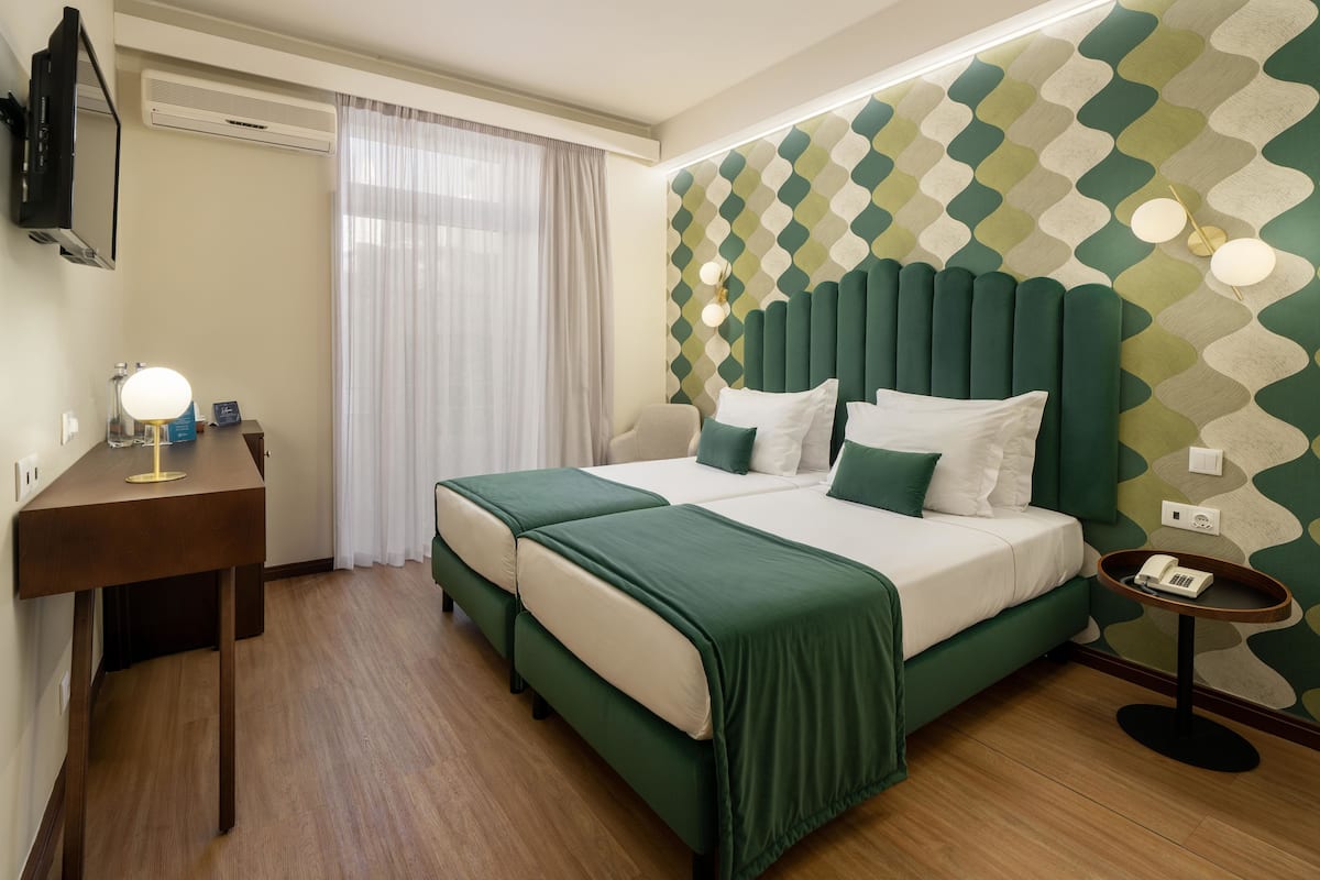 Ein Hotelzimmer mit zwei Betten, einem Nachttisch mit Lampe, einem Spiegel, einem Wandheizkörper, einem Telefon und einer Wand mit Muster.