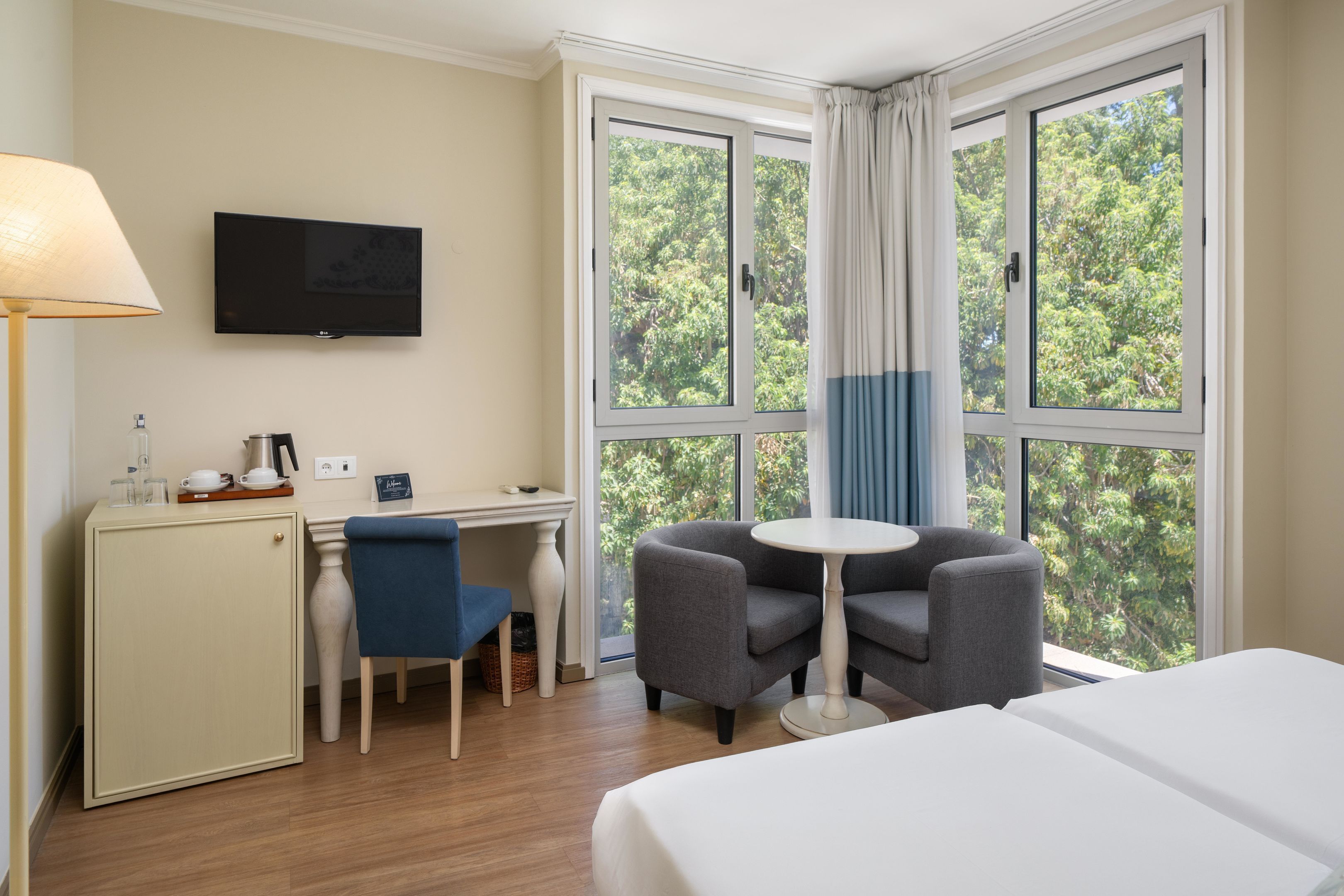 A hotel room with a bed, a desk with a chair, a television, and a window with curtains.