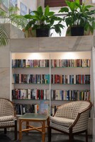 Eine Bibliothek mit Bücherregalen, zwei gemusterten Sesseln, einem kleinen Tisch und Topfpflanzen.