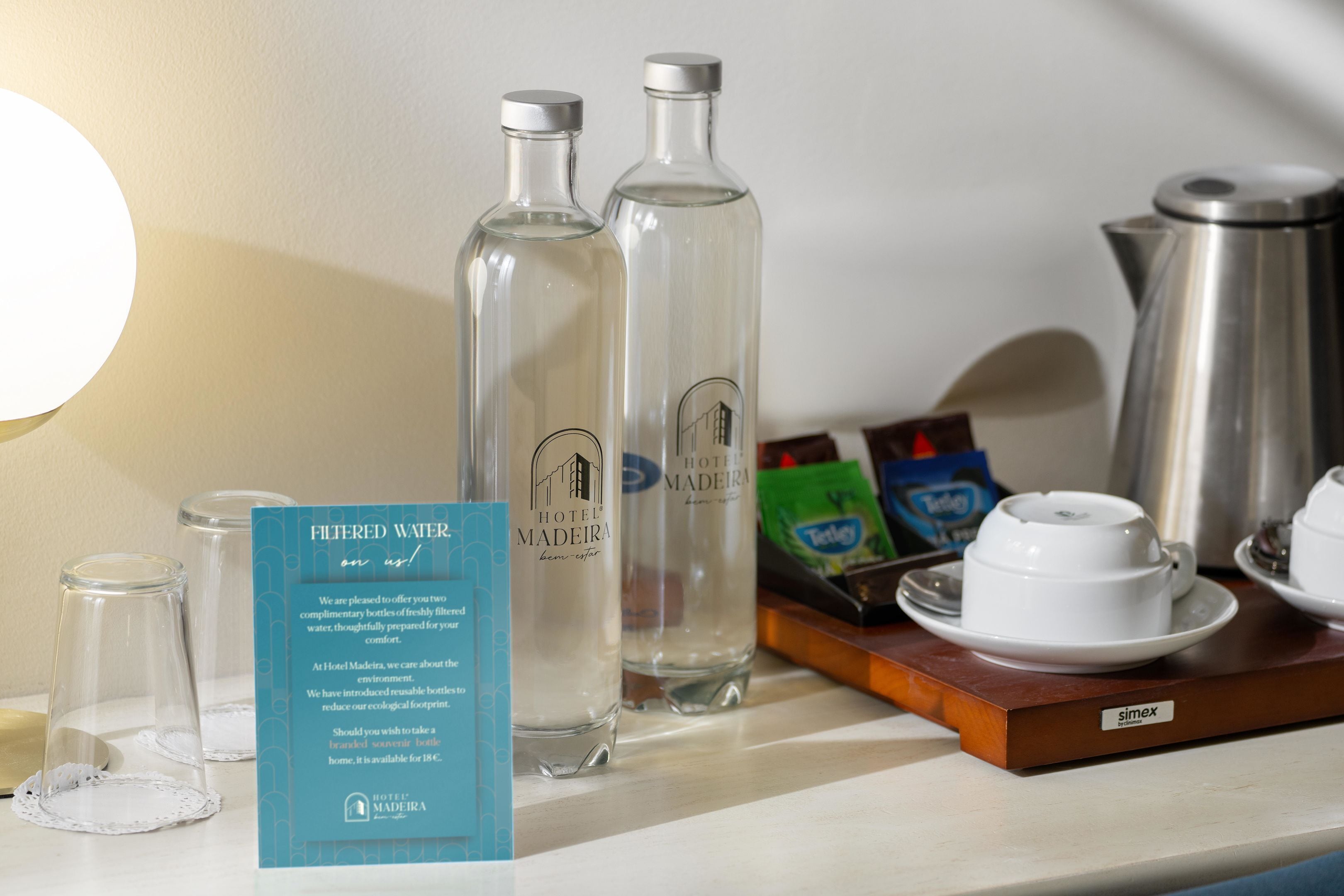 A hotel minibar with two bottles of Hotel Madeira water, a coffee maker, and a tea bag.