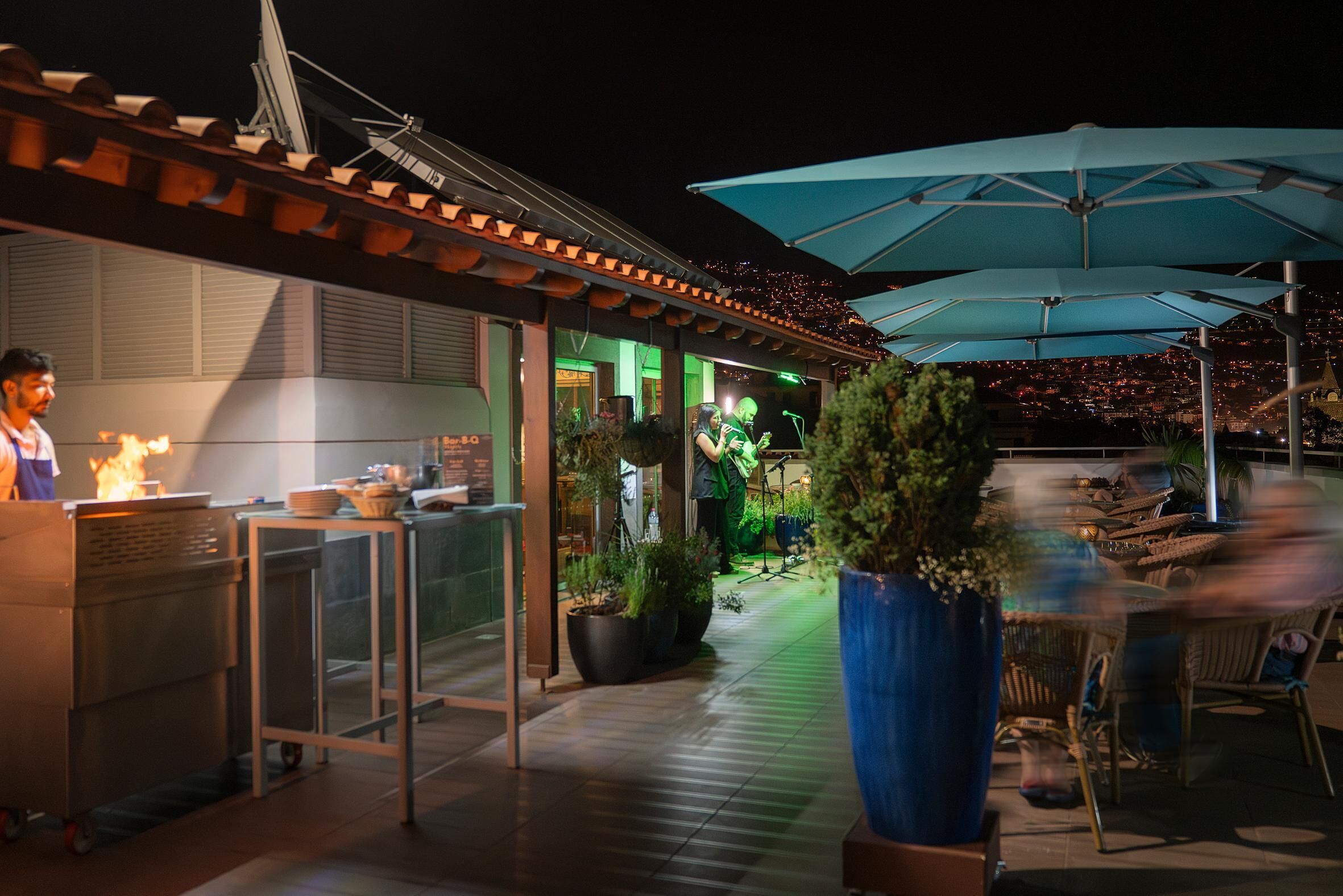 An outdoor dining area with umbrellas, a kitchen, and a view of the city at night.