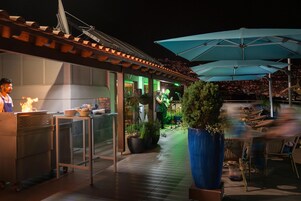 An outdoor dining area with umbrellas, a kitchen, and a view of the city at night.