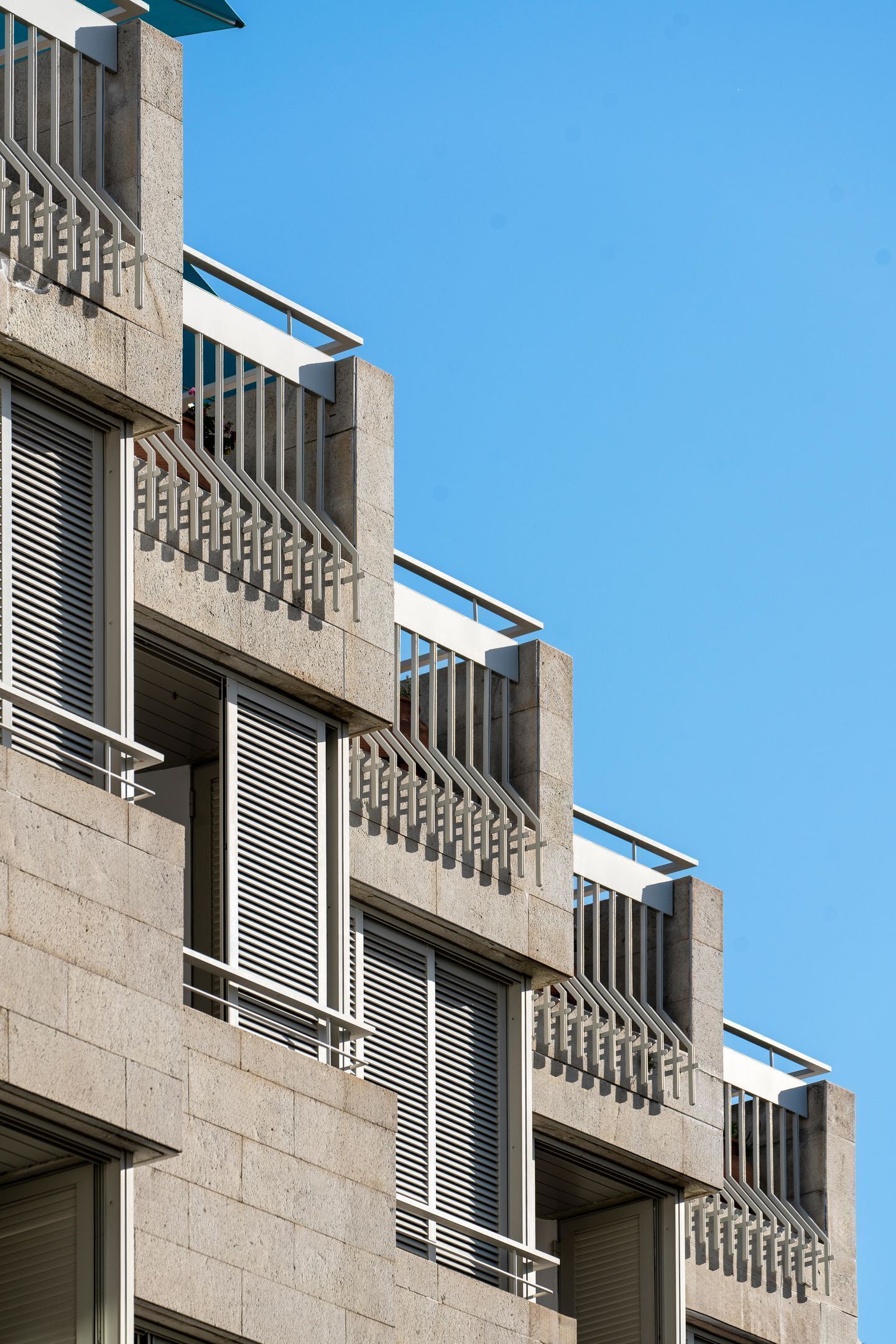 A modern building with multiple balconies, large windows, and a clear blue sky.