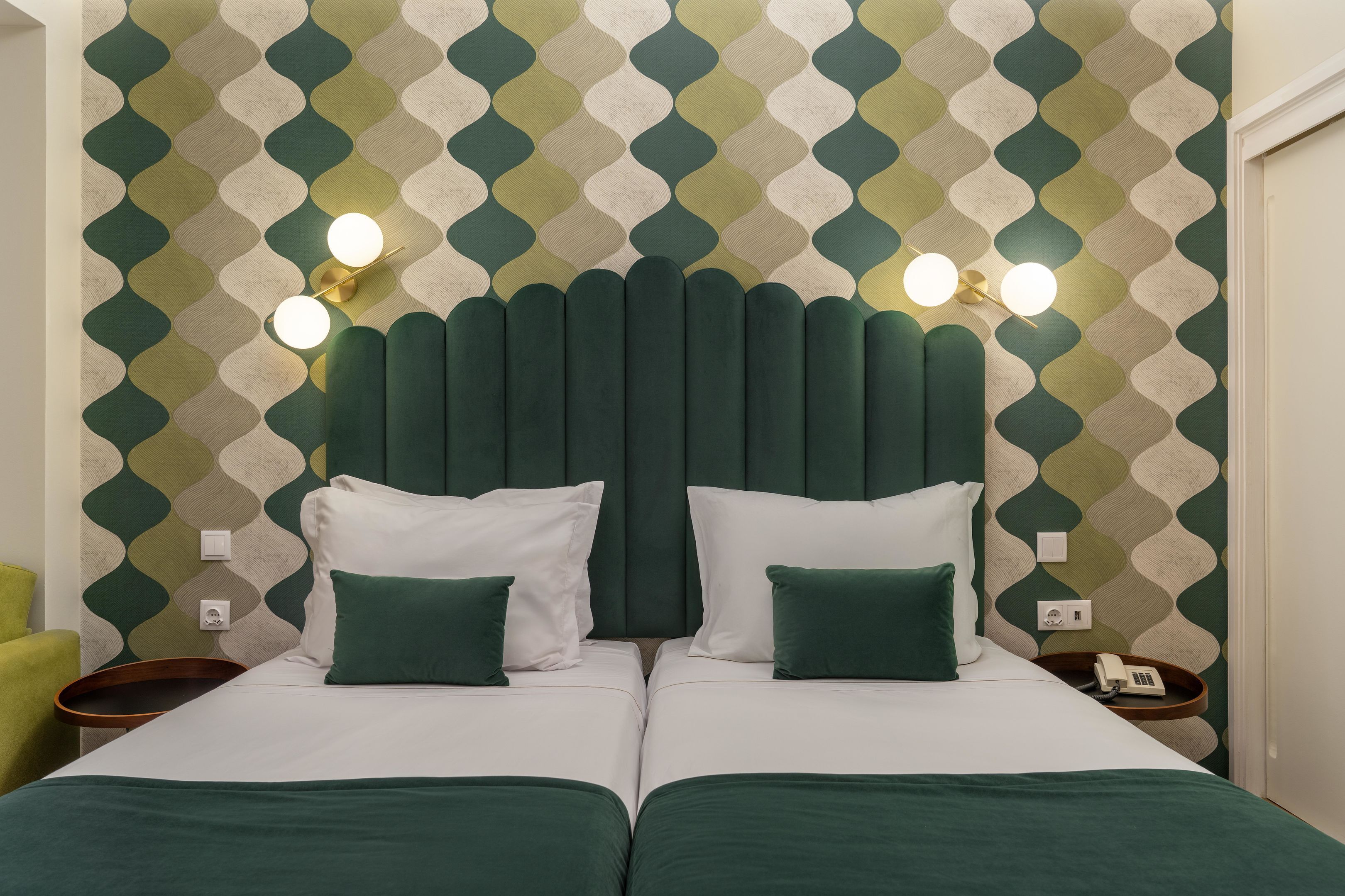 Een tweepersoonsbed met groen beddengoed, een hoofdbord met een bijzonder ontwerp en twee bedlampjes.