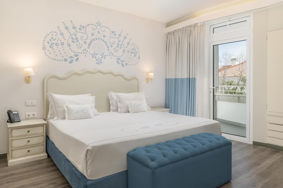 Ein ordentlich eingerichtetes Schlafzimmer mit einem großen Bett, Nachttischlampen, einem Telefon am Nachttisch und einem Fenster mit Vorhängen.