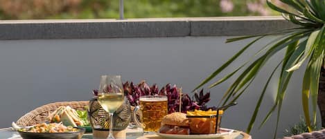 A balcony with wicker furniture, a table set with food and drinks, and a view of a cityscape with a clock tower.