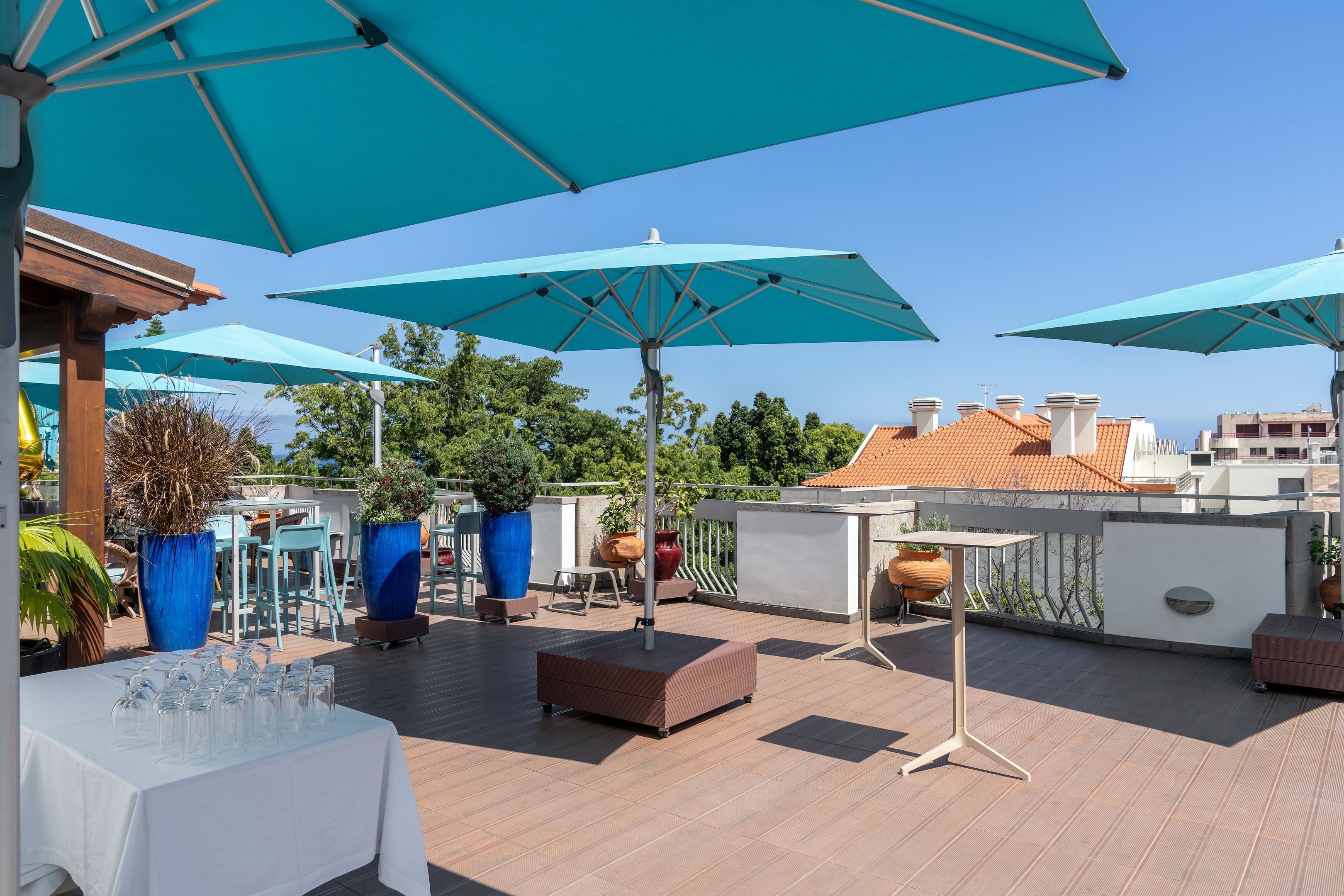 Eine Dachterrasse mit mehreren blauen Sonnenschirmen, Sitzgelegenheiten und Blumentöpfen.