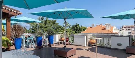 Een terras op het dak met meerdere blauwe parasols, zitgedeeltes en potplanten.