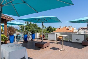 A rooftop terrace with multiple blue umbrellas, seating areas, and potted plants.
