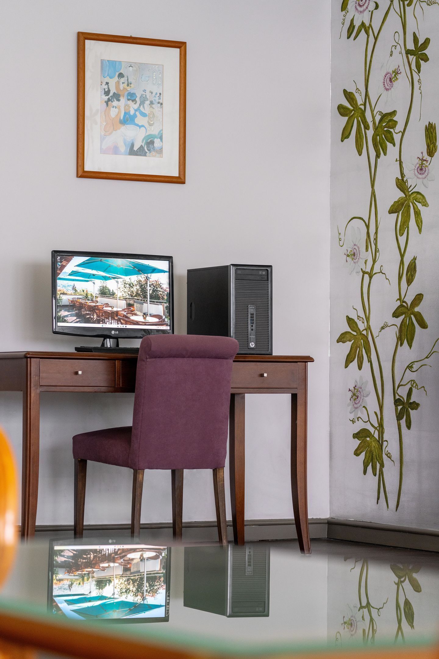 Una stanza con una scrivania in legno, una sedia viola, un quadro appeso al muro e una pianta decorativa sulla destra.