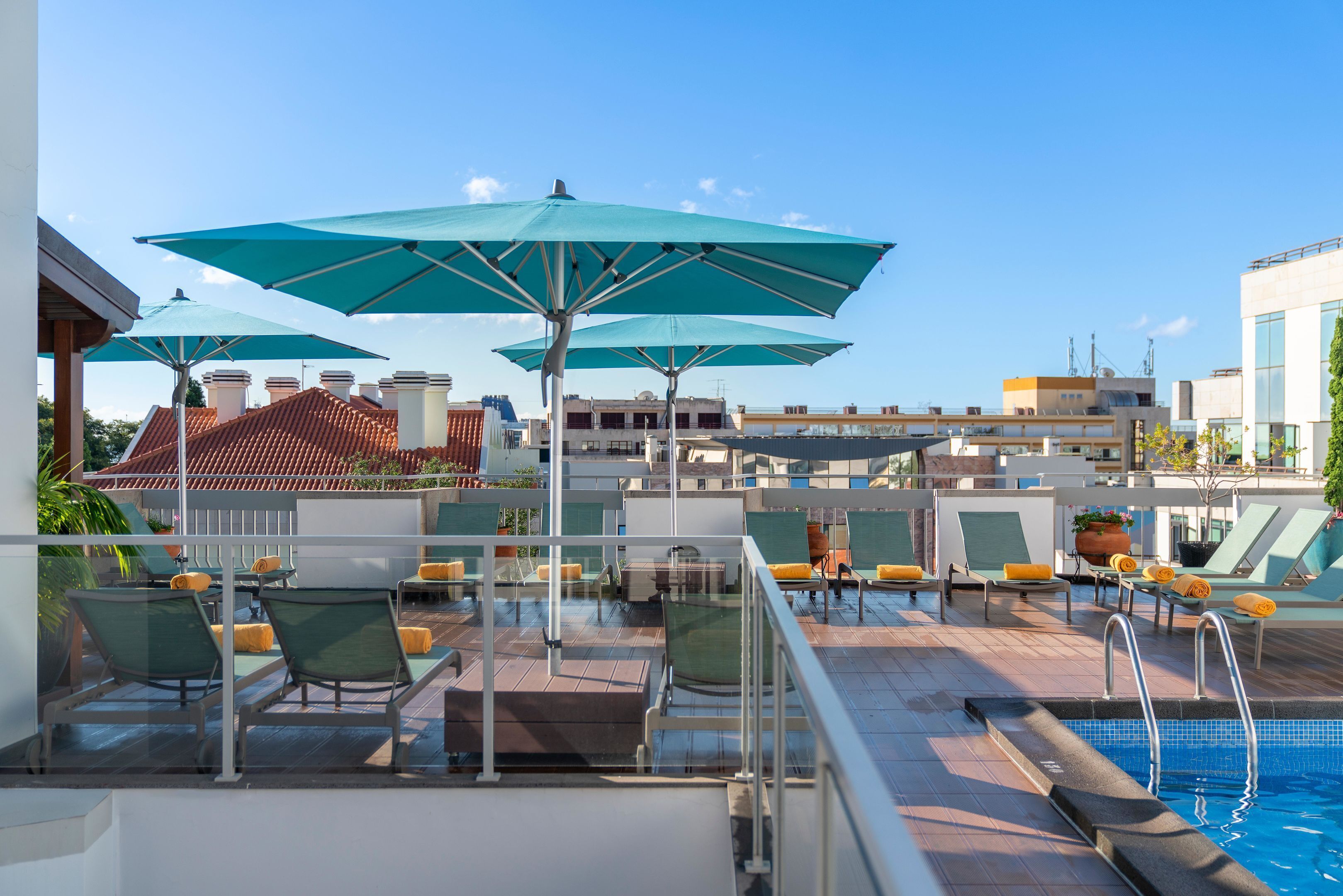 A rooftop pool area with lounge chairs, umbrellas, and a swimming pool.