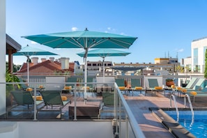 A rooftop pool area with lounge chairs, umbrellas, and a swimming pool.