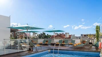 Una piscina al aire libre, sombrillas, sillones reclinables de piscina