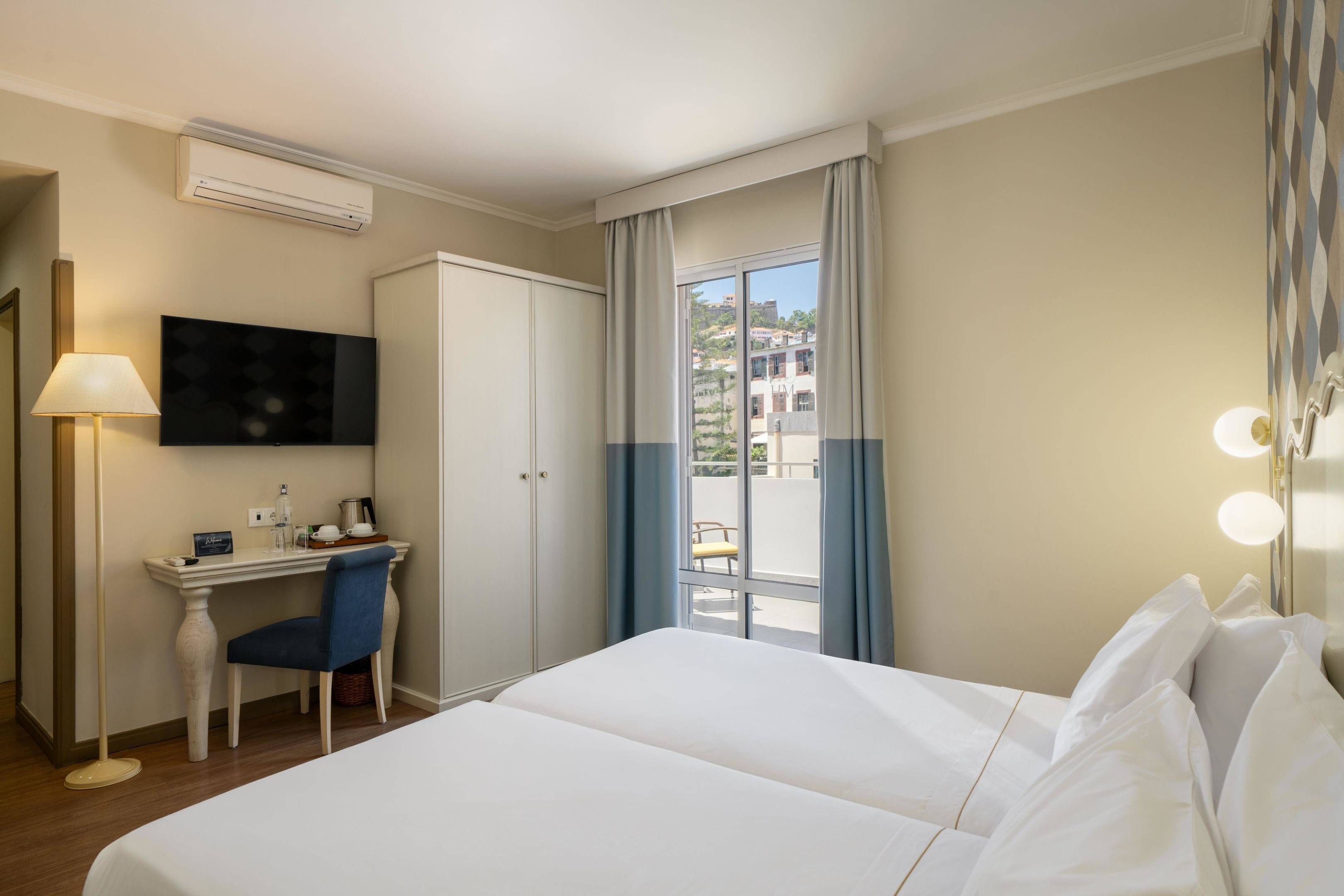 Ein Hotelzimmer mit Bett, Schreibtisch, Stuhl, Fernseher und Blick ins Freie.