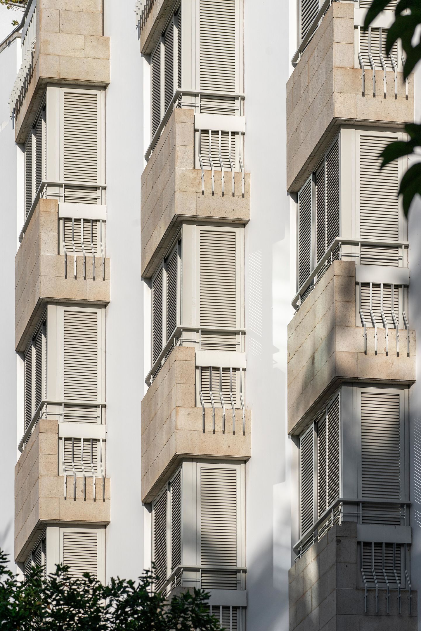 A multi-story building with a modern architectural style, featuring a series of balconies with metal railings and horizontal window blinds.