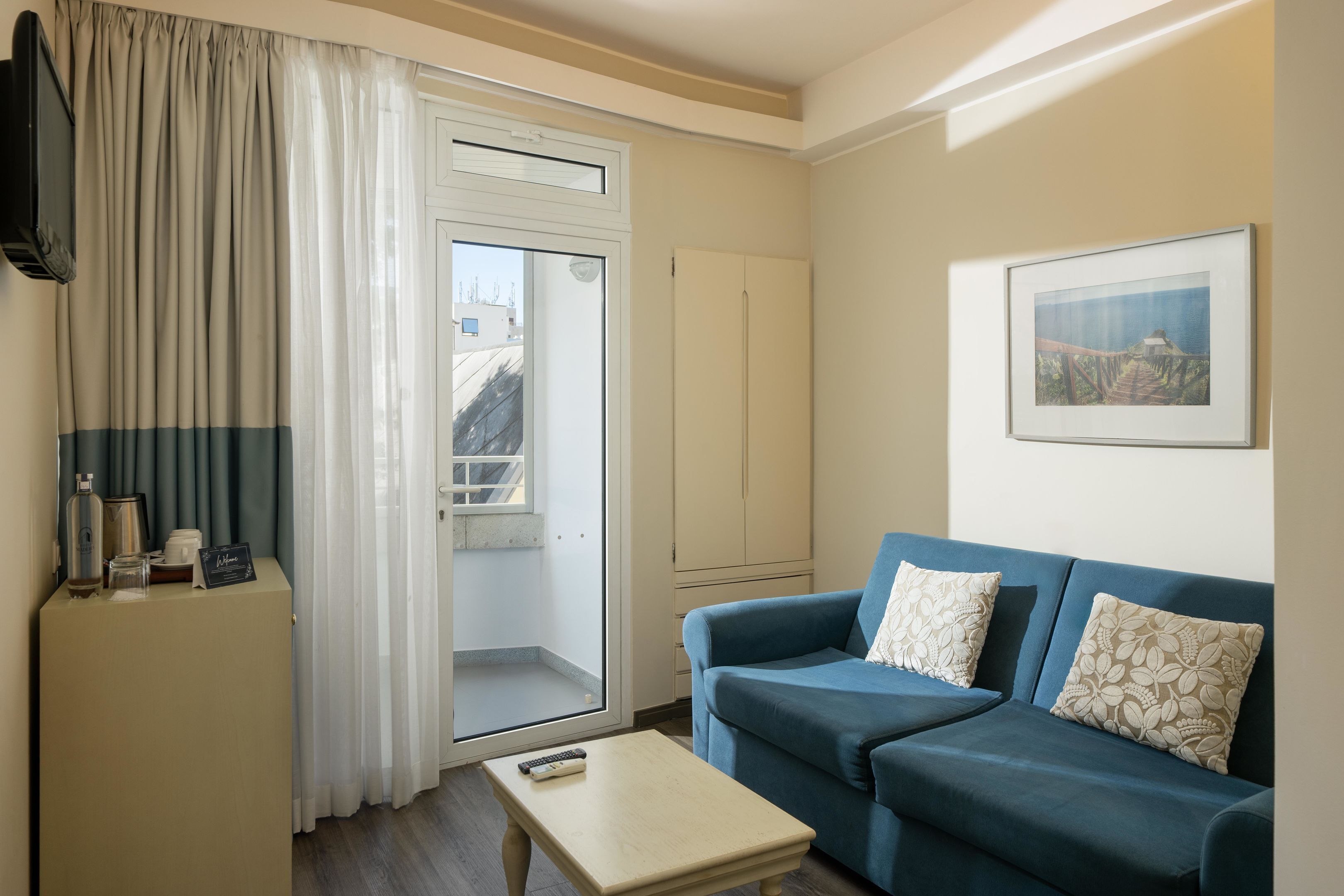 A living room with a blue sofa, a small table, a cabinet, a TV, and a door leading to a balcony.