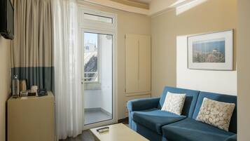 A living room with a blue sofa, a small table, a cabinet, a TV, and a door leading to a balcony.