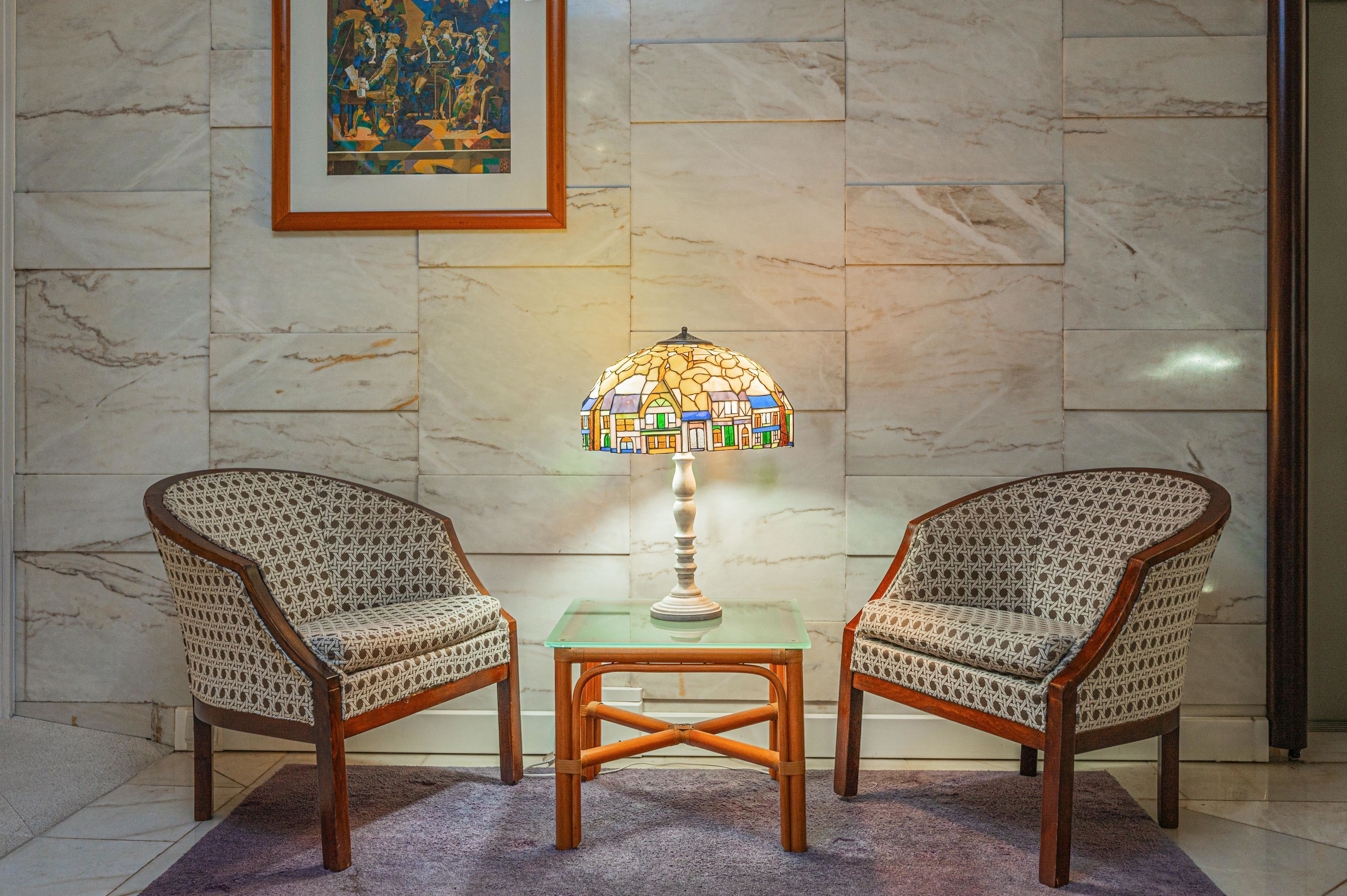 Deux fauteuils en osier, une table en verre et une lampe à motifs de mosaïque placés entre eux.