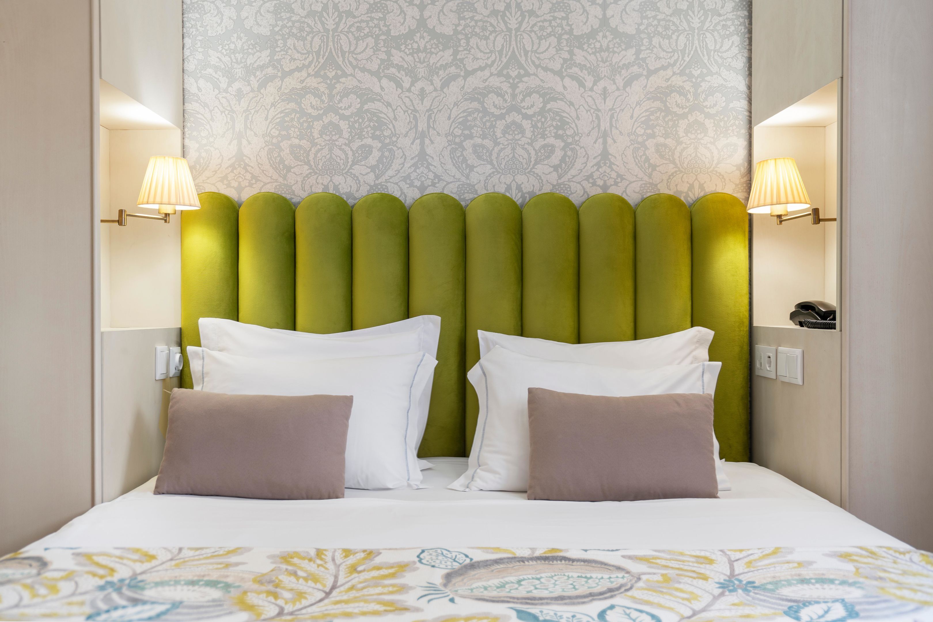 A neatly made bed with a patterned bedspread, a green upholstered headboard, and two bedside lamps.