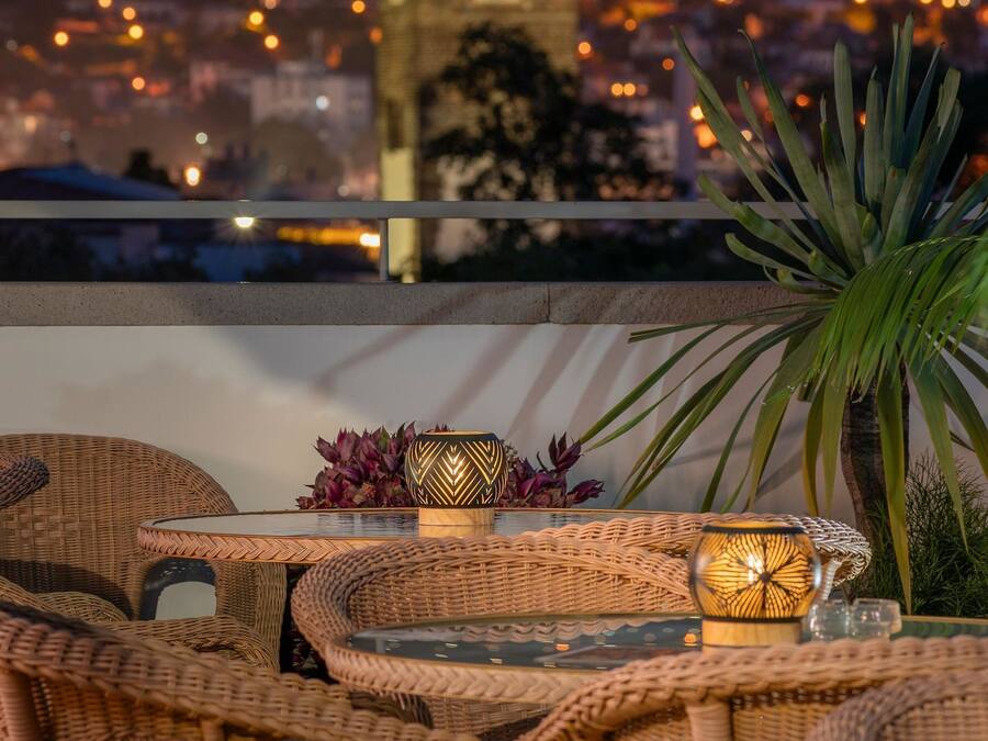 A balcony with wicker furniture and a table, overlooking a cityscape at night.