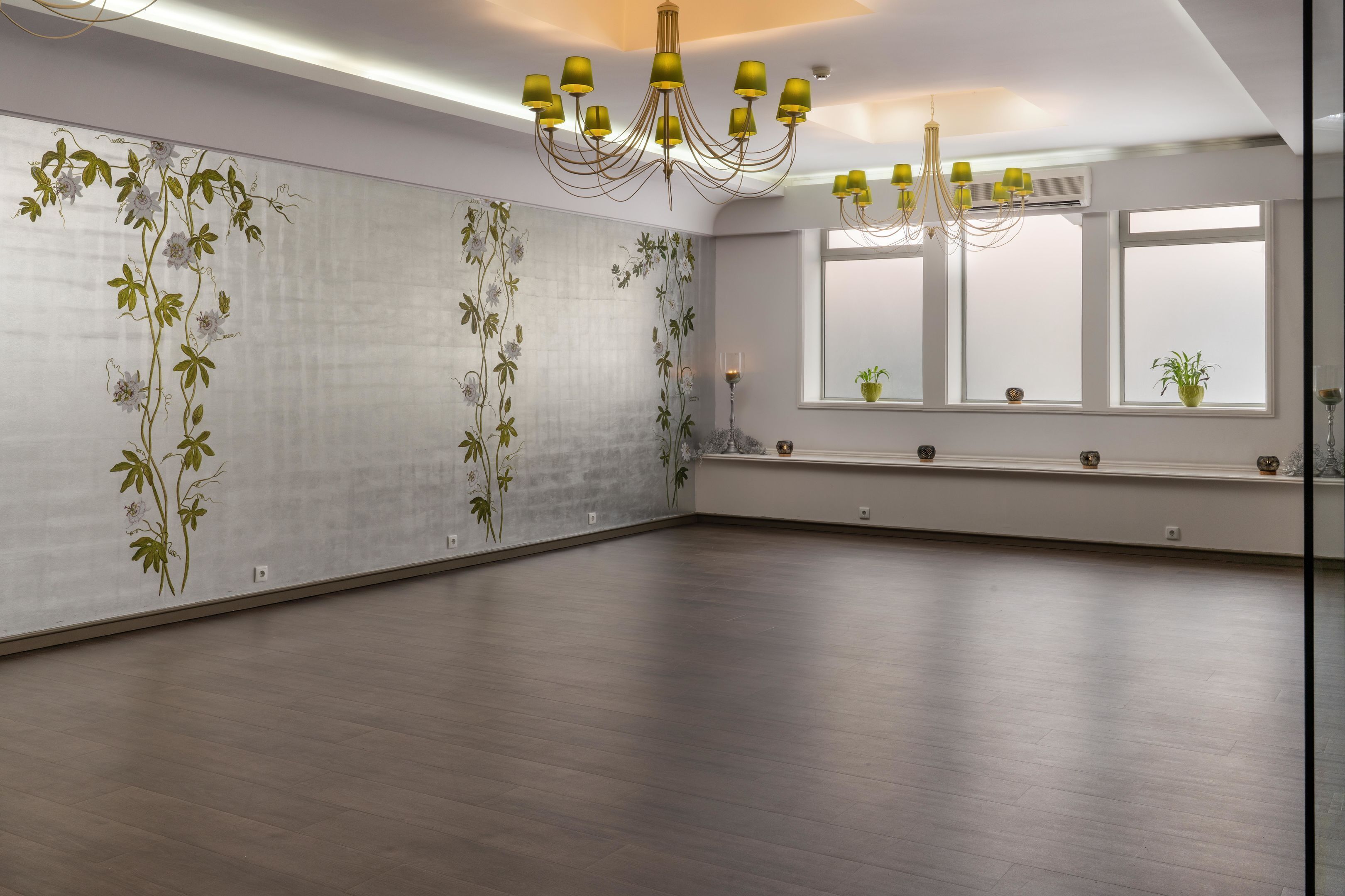 Ruime kamer met een groot raam, een kroonluchter en een wand met bloemenbehang.