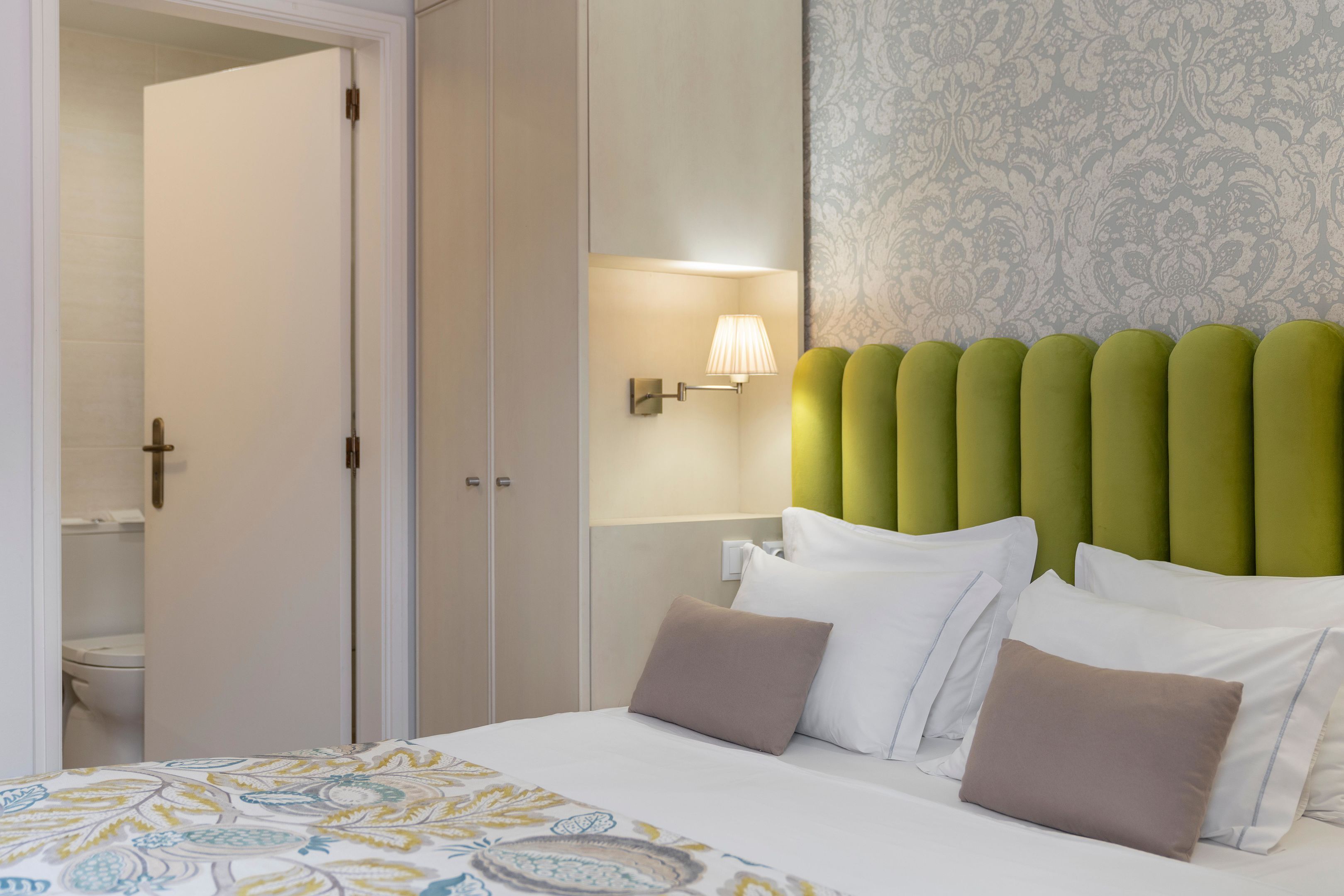 A hotel room with a bed, a nightstand, a wall-mounted lamp, and a patterned wallpaper.