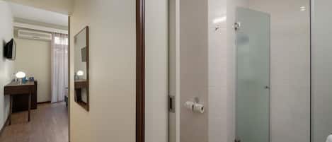 A hotel bathroom with a glass shower door, a toilet paper holder, and a mirror.