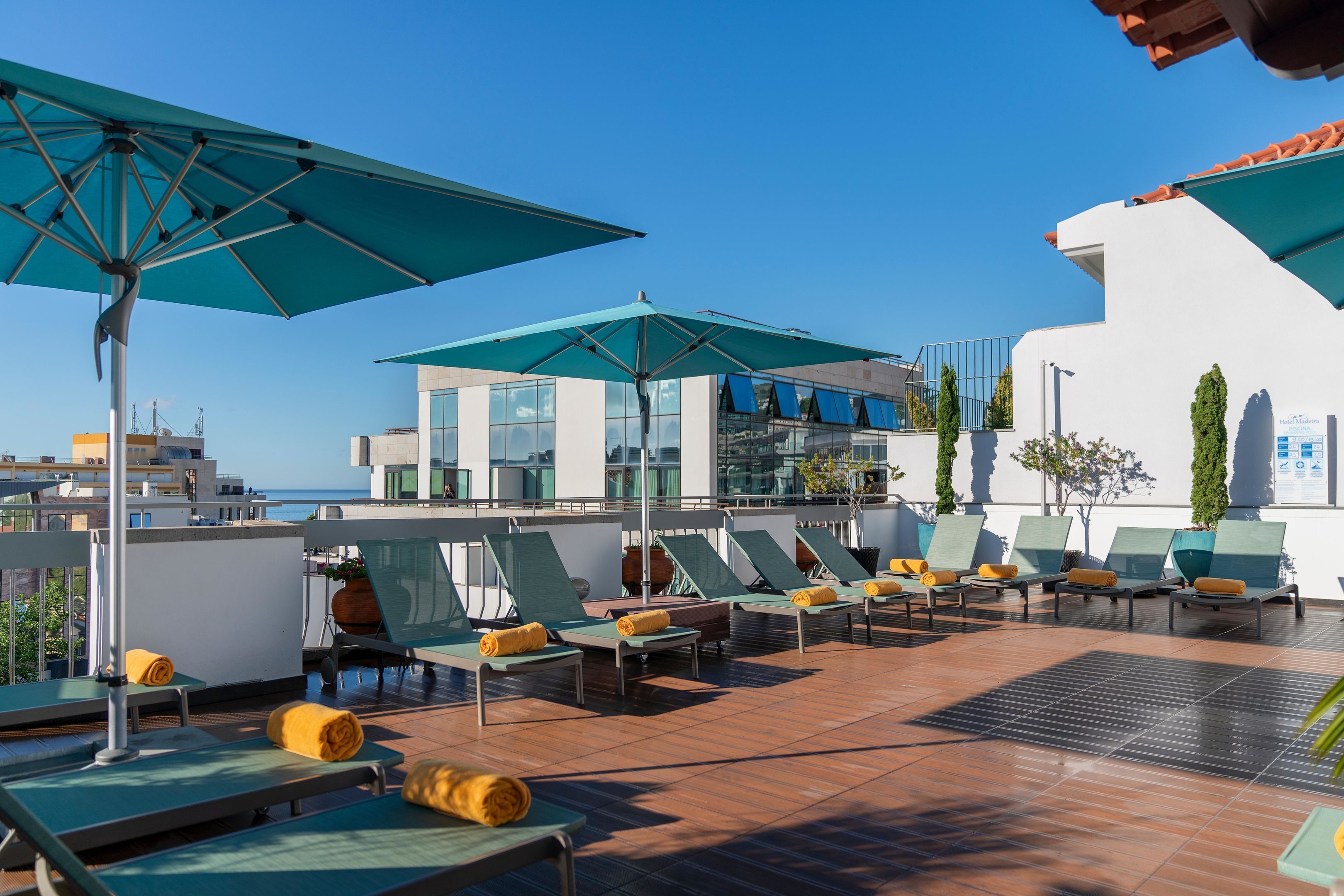 Un área de lounge en la azotea con sillones de sol, sombrillas y vistas a la ciudad.