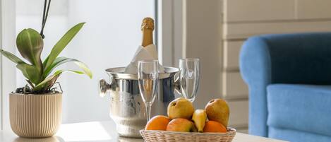 A table with a potted orchid, a champagne bottle, two glasses, and a basket of fruit.