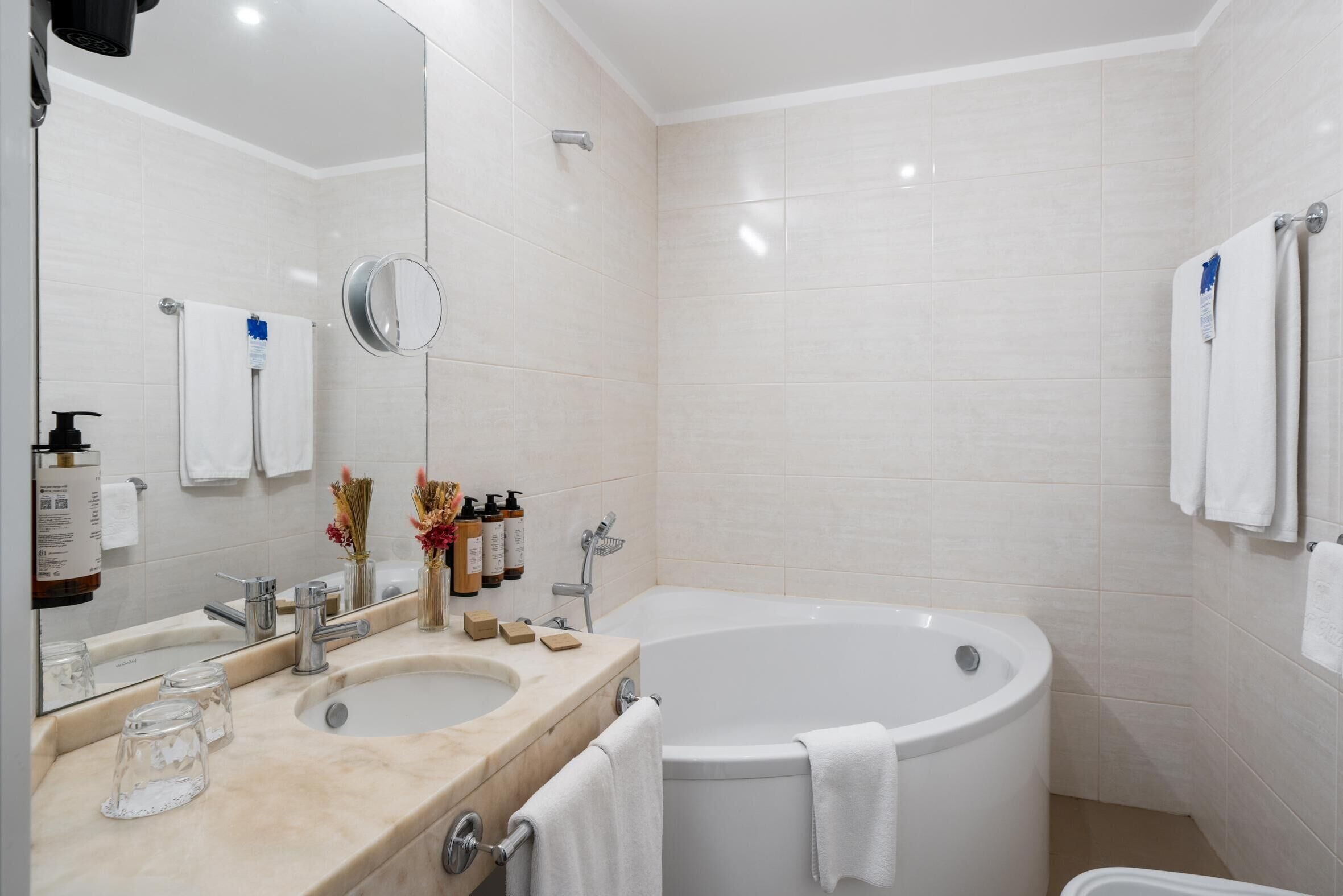 A modern bathroom with a large bathtub, two sinks, a mirror, and toiletries.