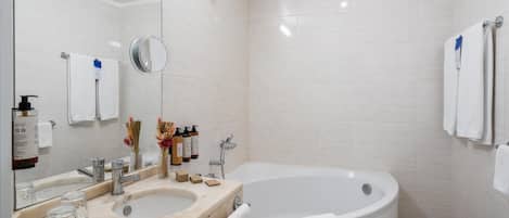 A modern bathroom with a large bathtub, two sinks, a mirror, and toiletries.