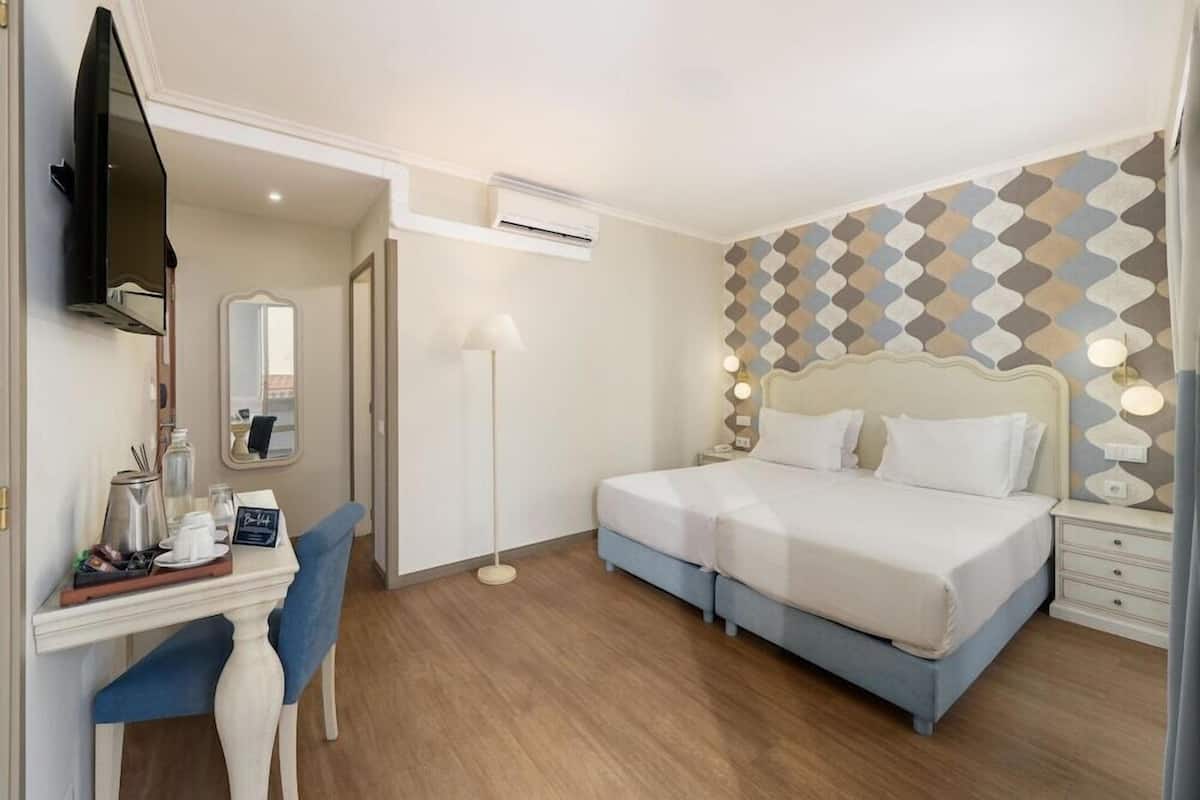Ein Hotelzimmer mit Bett, Nachttischen, einem Schreibtisch mit Stuhl, einem Flachbildfernseher, einem Spiegel und einer Wand mit Muster.