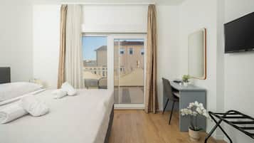 Habitación de hotel con cama, escritorio, silla, televisor y balcón con vista a edificios.