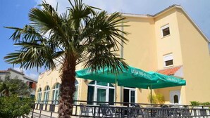 Ένα κτίριο με πράσινη τέντα, εξωτερικό χώρο για καθίσματα και ένα φοινικόδεντρο.