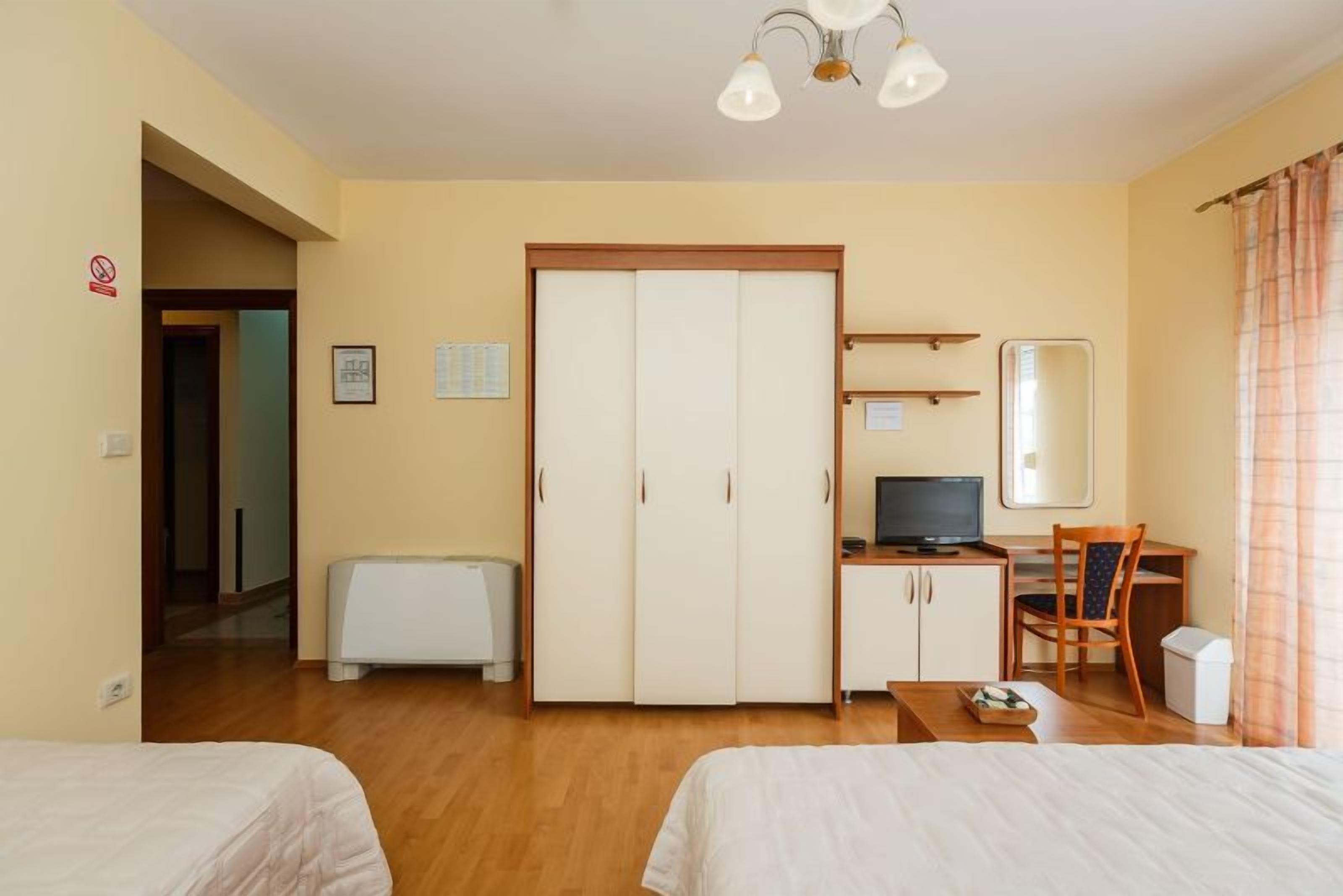 A hotel room with two beds, a desk with a computer, a wardrobe, and a television.