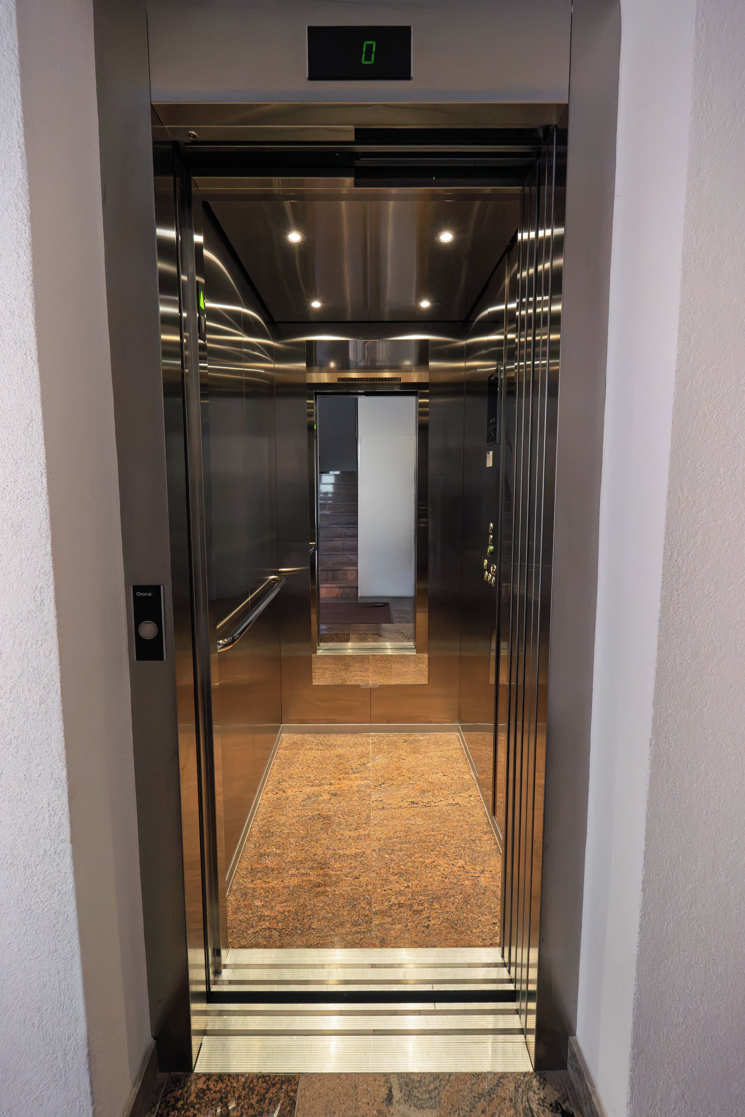 An elevator with a metallic finish, a digital display at the top, and a carpeted floor.
