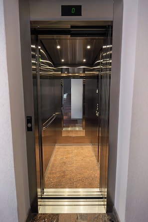 An elevator with a metallic finish, a digital display at the top, and a carpeted floor. - Adria (Kastela)