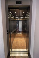 An elevator with a metallic finish, a digital display at the top, and a carpeted floor.