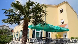 A building with a green awning, outdoor seating, and a palm tree. - Adria (Kastela)